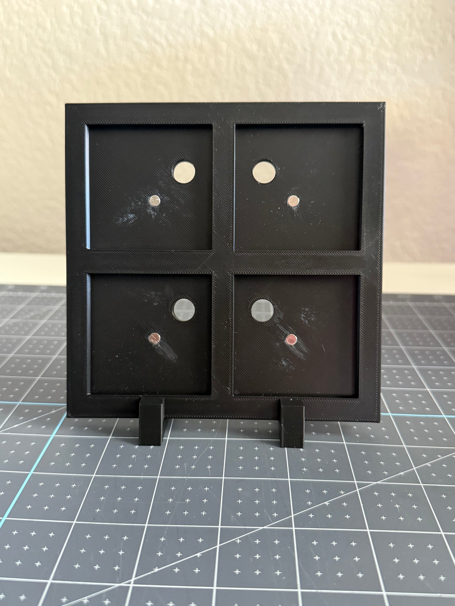 Black display stand with four square compartments for magnets.